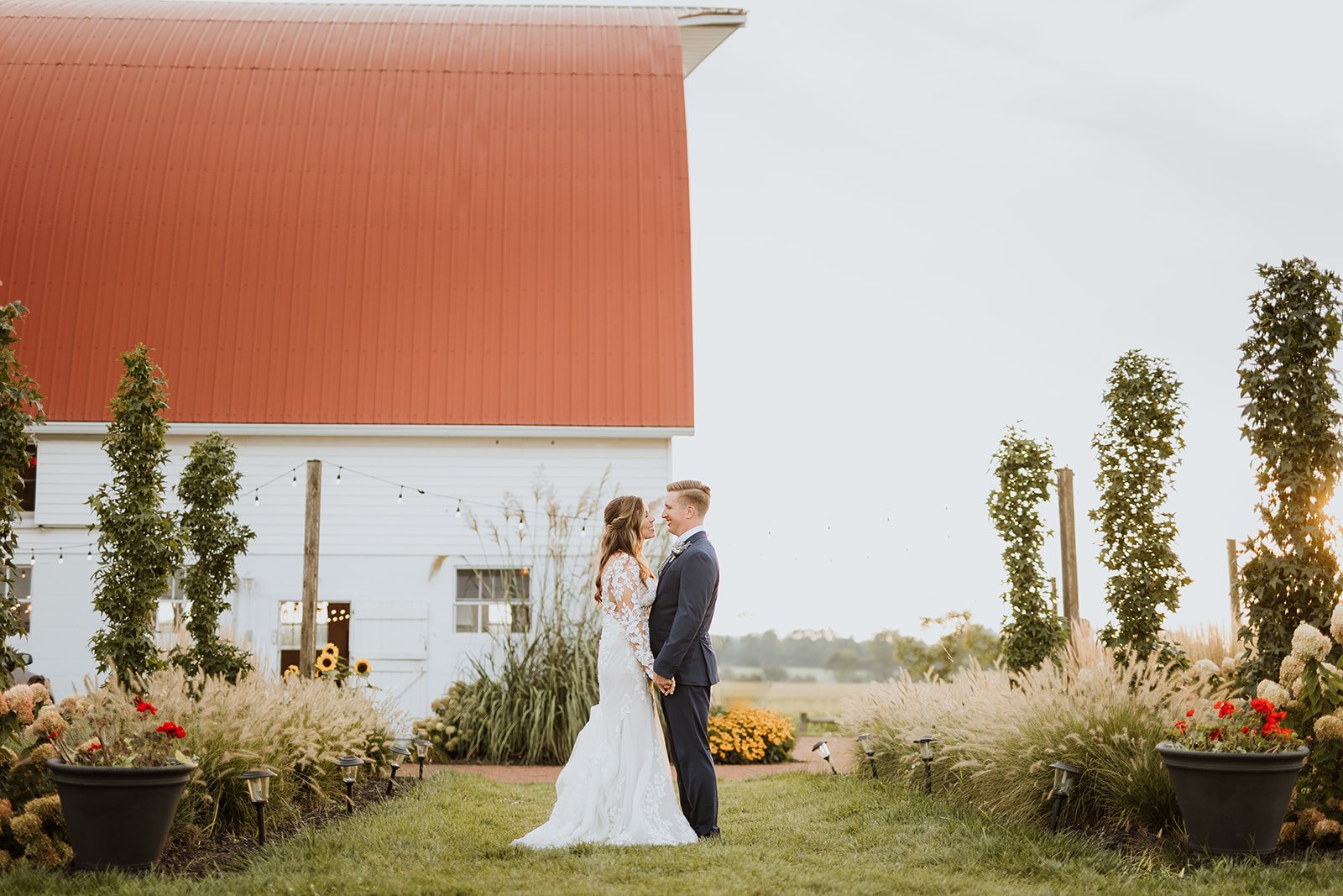 Couple holds hands on the garden path in front of the white barn.