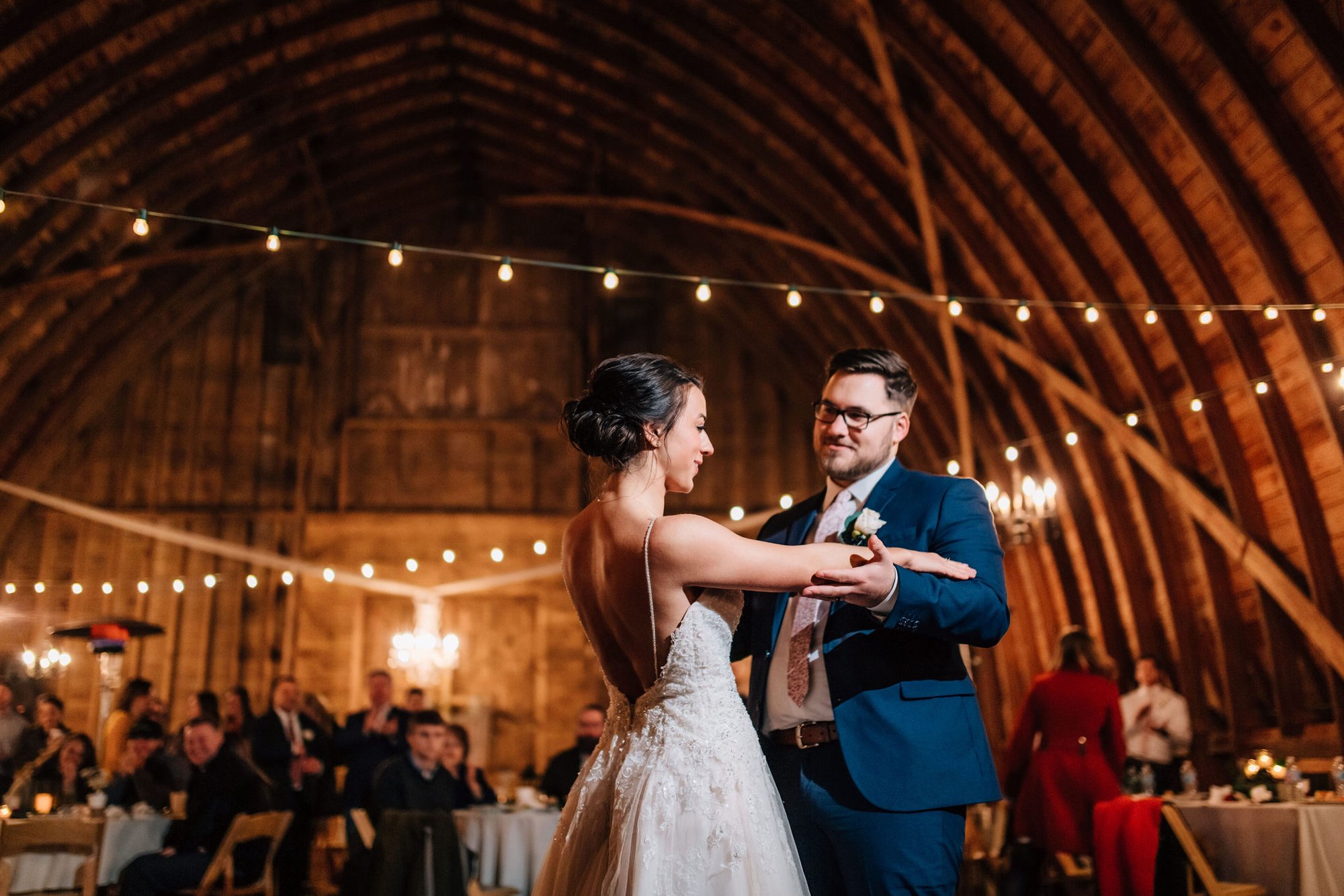Bride and groom dance beneath the barn's arched rafters and string lights.