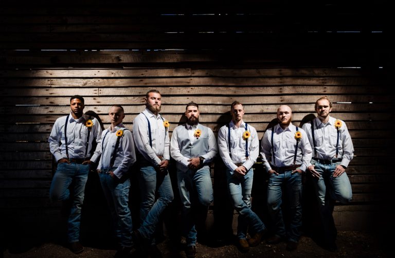 The groom's party in white shirts and suspenders against the slatted corn-crib wall.