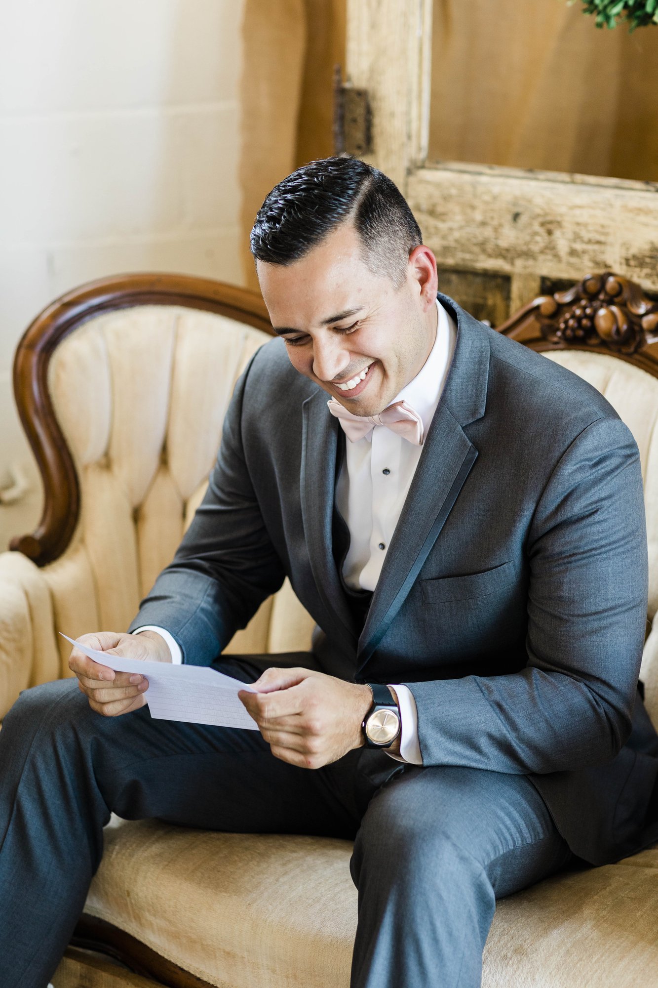 Groom seated on an antique settee reading a note before the ceremony